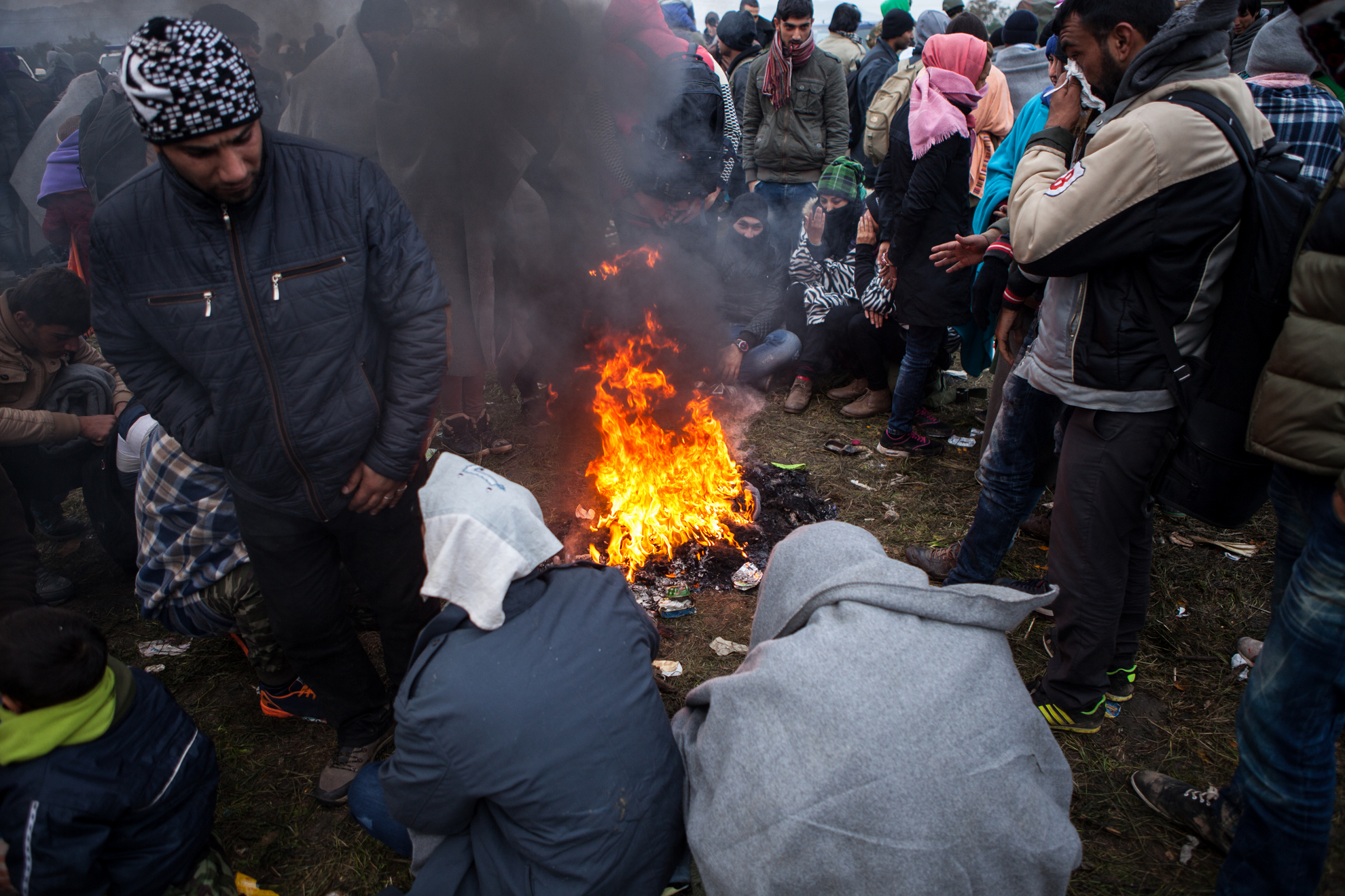 Begunci v Rigoncah čakajo na 12km dolgo pot do zbirnega centra v Brežicah. Med čakanjem se begunci grejejo ob ognju.